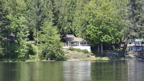 Un chalet au bord du lac, doté d’une grande terrasse et entouré d’une forêt dense.