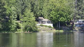 A lakeside cabin with a large deck, surrounded by dense forest.