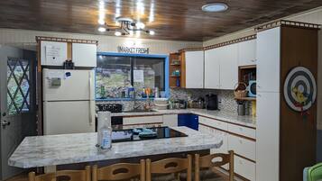 A kitchen with a marble countertop, wooden chairs, a refrigerator, a sink, and cabinets.