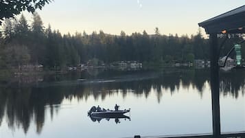 A tranquil lakeside view from a deck with a boat docked, surrounded by trees and buildings.