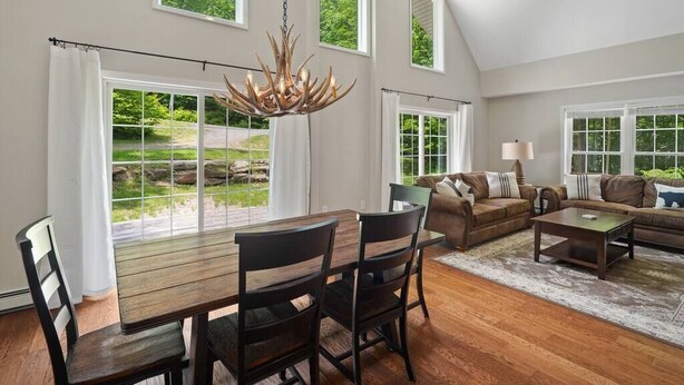 A spacious living room with a dining area, large windows, and a chandelier.