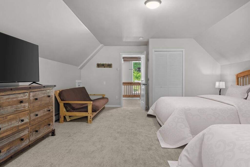 A bedroom with two beds, a wooden dresser, a television, and a view of the outdoors.