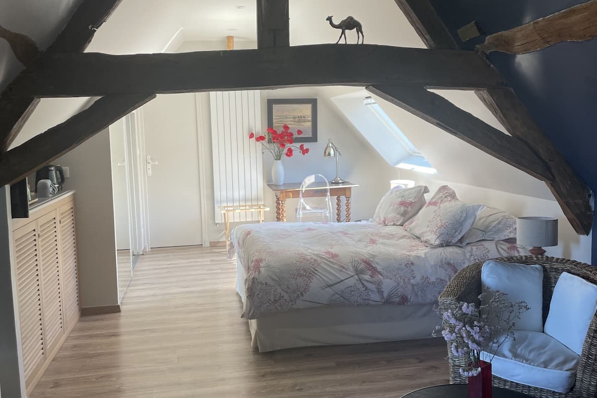 A bedroom with a bed, a chair, a table, and a desk. There is a window with a view of the outside.