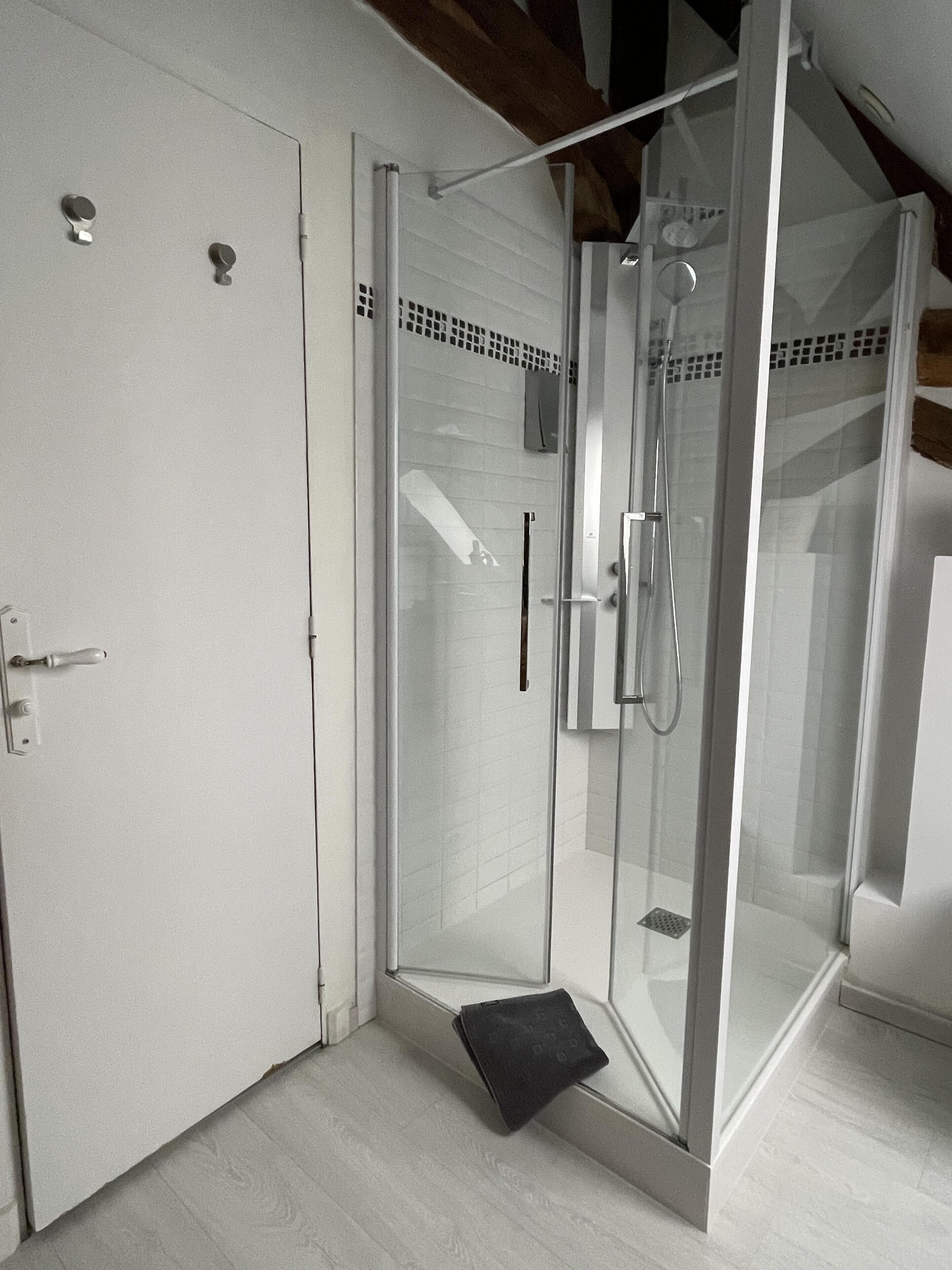 A modern bathroom with a glass-enclosed shower, a white door, and a wooden floor.