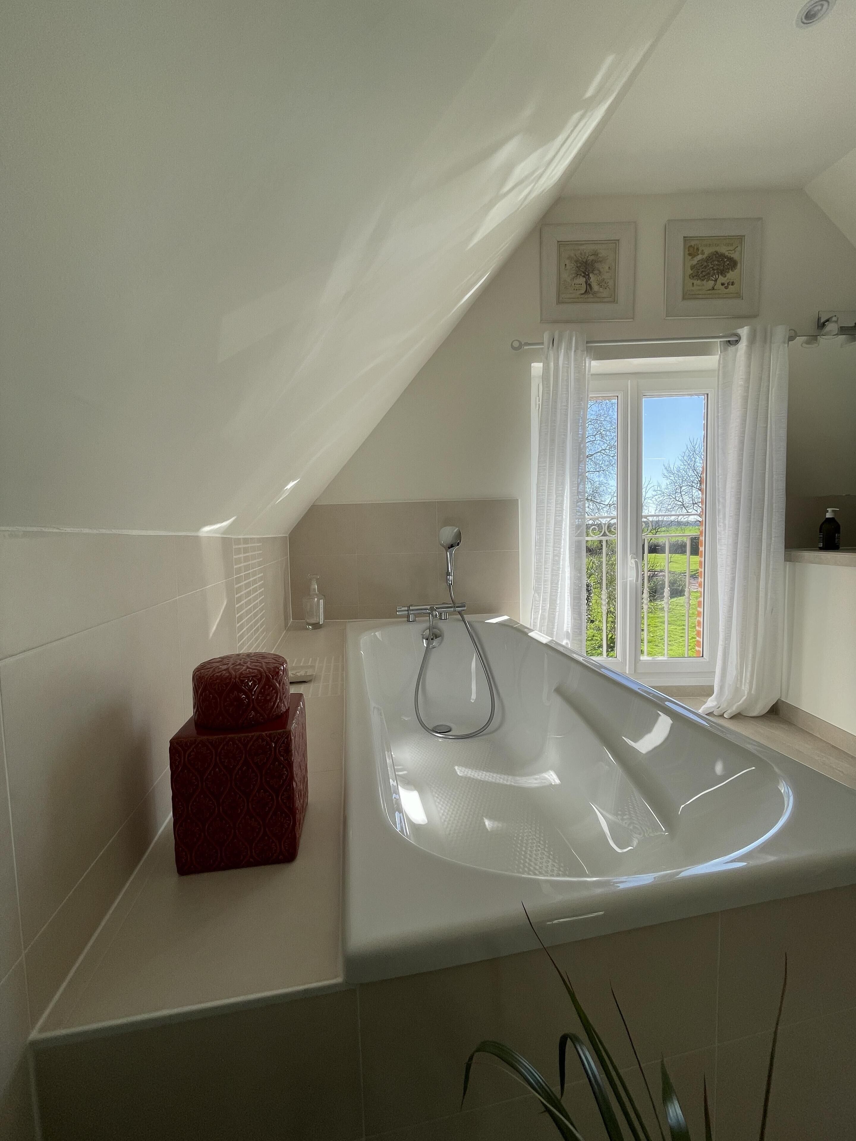 Een moderne badkamer met een vrijstaand bad, een douche en een raam met gordijnen.
