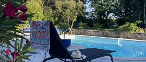 A poolside area with a lounge chair, a decorative umbrella, and a sign.