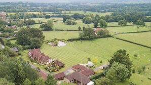 A rural landscape with a large green field, a pond, and a cluster of houses with red roofs. - Motor House Loft - beautiful loft conversion in lovely rural location by Bloom Stays (Sandhurst)