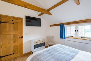 A bedroom with a bed, a dresser, a television, and a window with curtains.