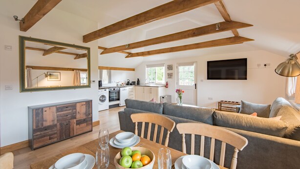 A spacious living area with a dining table set for four, a sofa, and a kitchen in the background. - Motor House Loft - beautiful loft conversion in lovely rural location by Bloom Stays (Sandhurst)