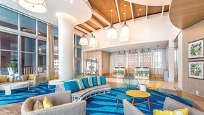 Un vestíbulo amplio con alfombra azul estampada, muebles modernos y ventanas grandes.