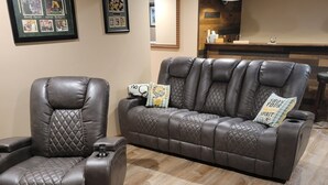 A living room with a leather recliner and sofa, a framed sports poster, and a wooden floor. - NFL Draft: Close to Lambeau and Appleton & Oshkosh airports. Sleeps  8+ (Appleton)