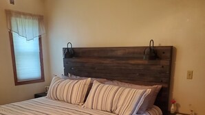 A bedroom with a large bed, a wooden headboard, a nightstand, and a window with blinds. - NFL Draft: Close to Lambeau and Appleton & Oshkosh airports. Sleeps  8+ (Appleton)