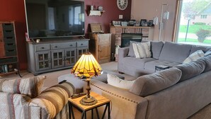A living room with a sofa, a TV, a lamp, and a window with a view of greenery. - NFL Draft: Close to Lambeau and Appleton & Oshkosh airports. Sleeps  8+ (Appleton)