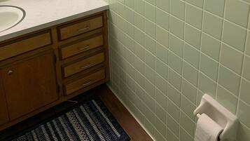 A bathroom with a white sink, wooden vanity, green-tiled walls, a mirror, decorative wall pieces, and a framed picture on the countertop.
