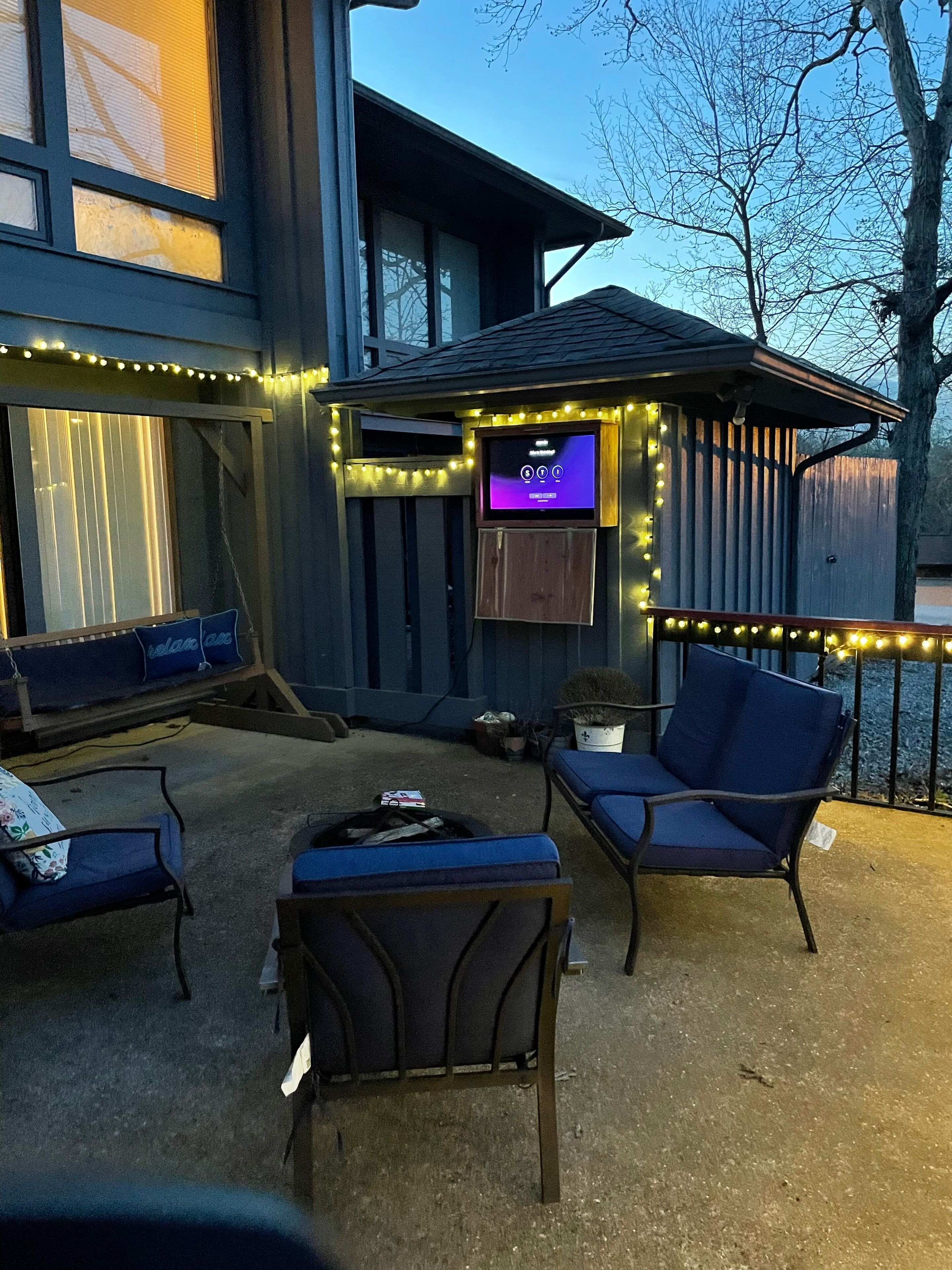 An outdoor seating area with a built-in TV, string lights, and a wooden deck.