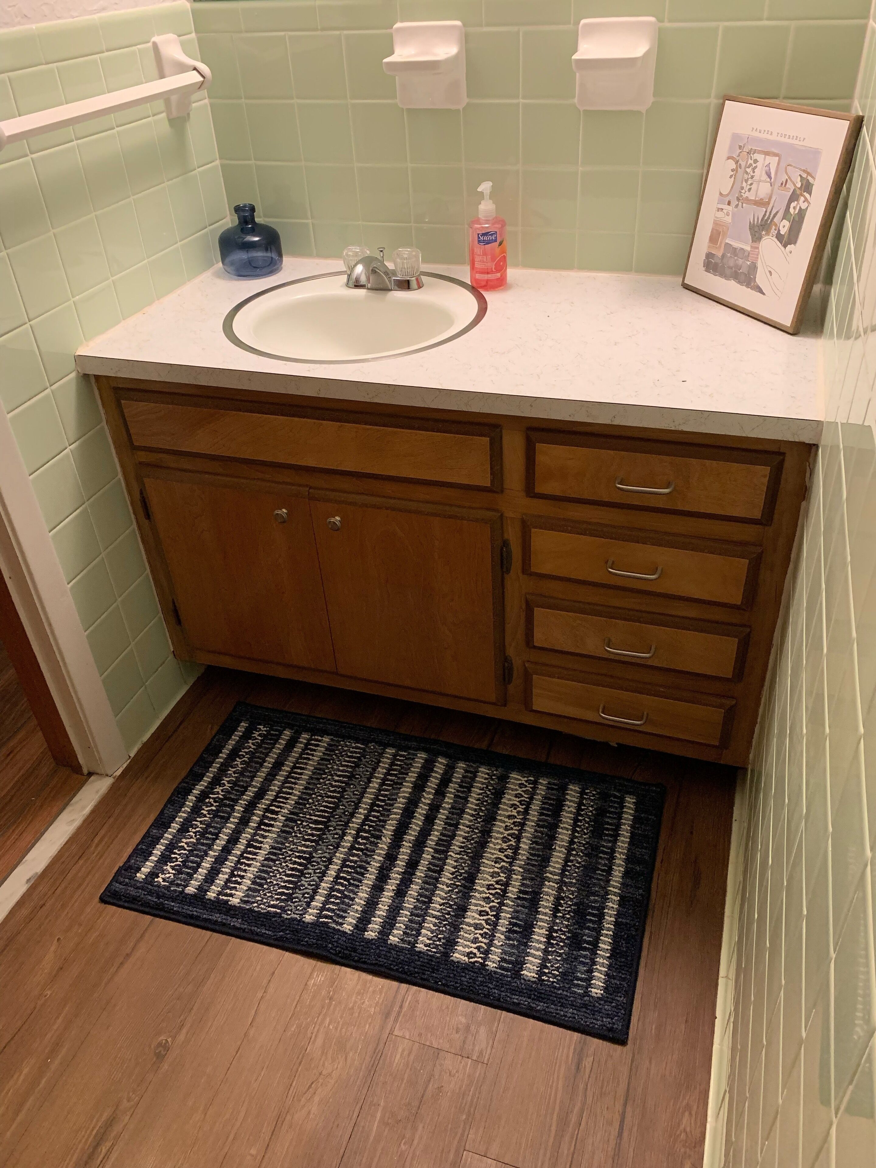 A bathroom with a wooden vanity, a sink, a mirror, a soap dispenser, and a framed picture on the wall.