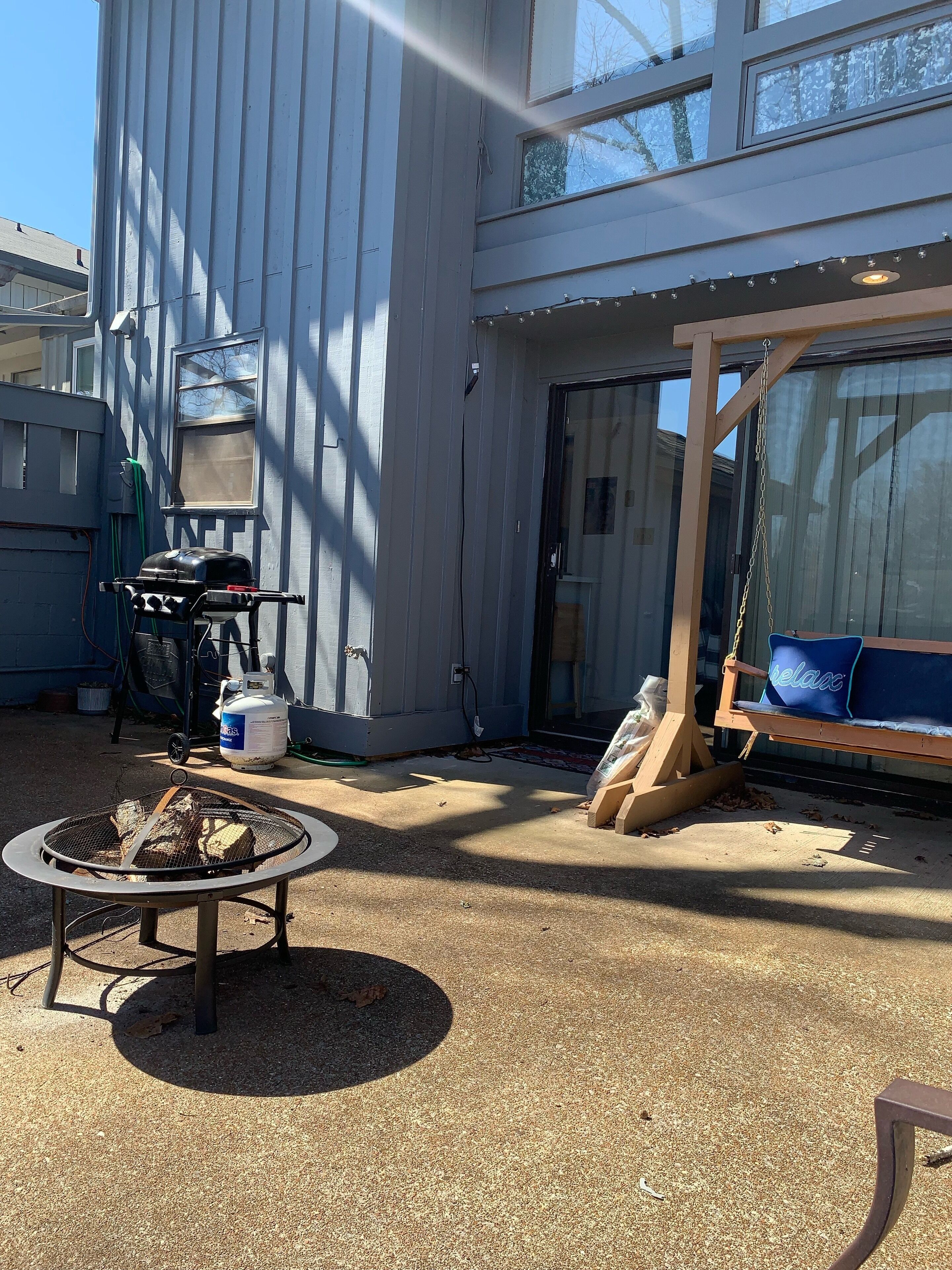 A backyard with a grill, a wooden swing, and a concrete patio.