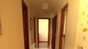 Um corredor estreito com um radiador à esquerda, uma porta no final e uma parede com padrão floral à direita.