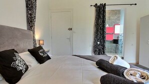A bedroom with a large bed, a nightstand, a door, and a view of a bathroom with a red cabinet. - 3-bedroom vacation home. Le Faou Aulne Maritime Crozon  (LE FAOU)