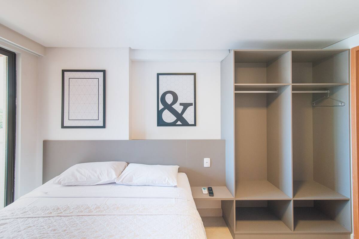 A bedroom with a bed, a nightstand, a wardrobe, and two framed pictures on the wall.
