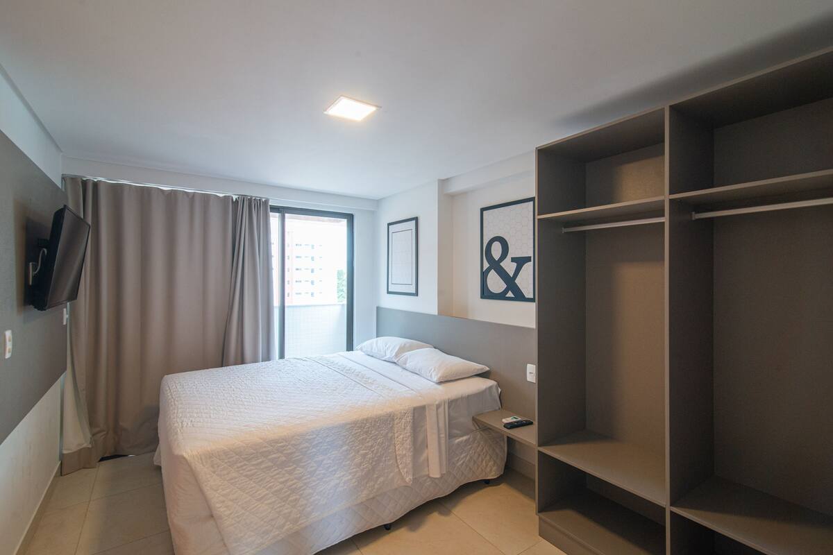 A hotel room with a bed, a bedside table, a TV mounted on the wall, and a large wardrobe.