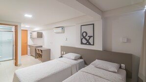 A hotel room with two beds, a desk, and a shower area. - GOLDFLAT Manaíra by Penareia.tur.br (João Pessoa)