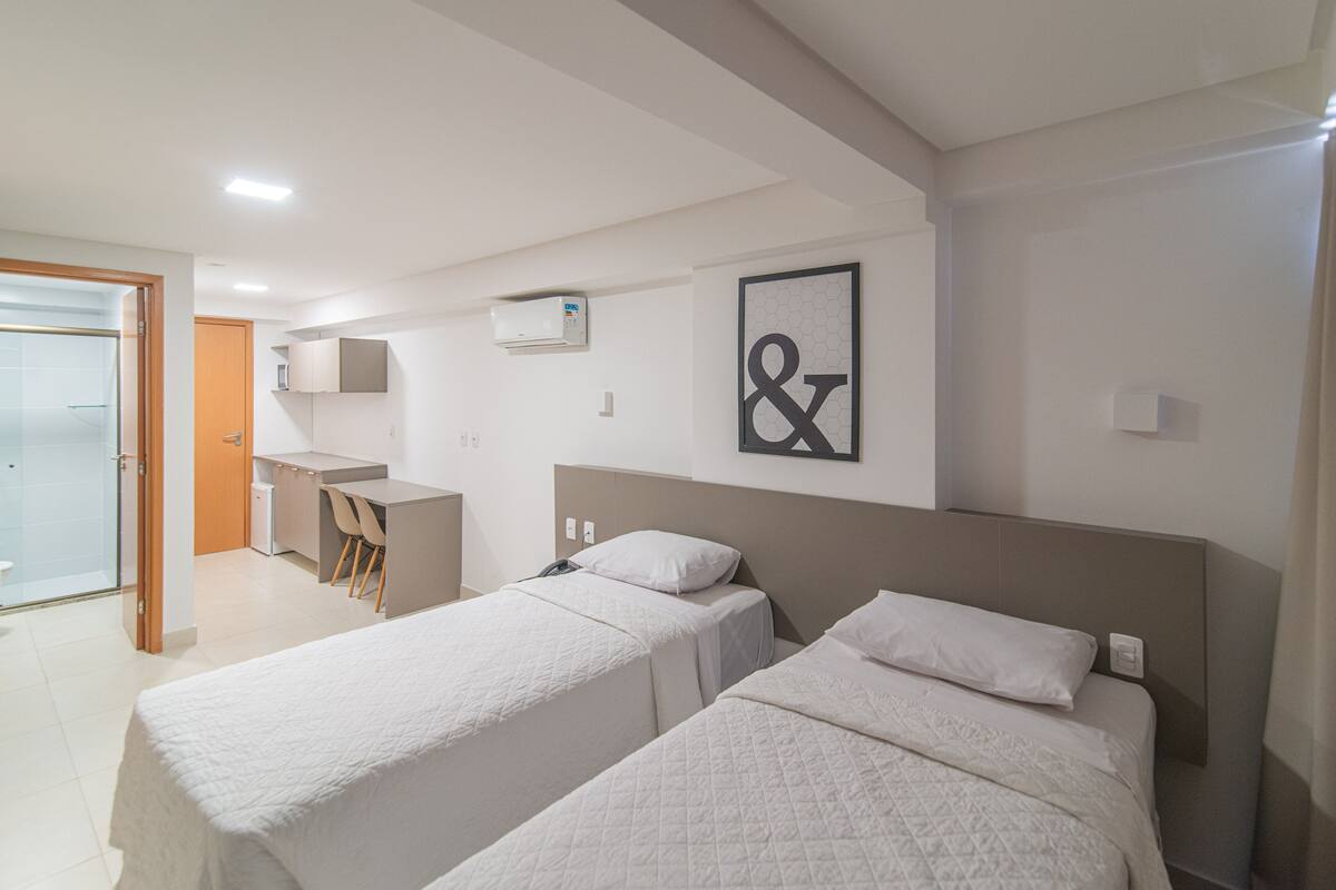 A hotel room with two beds, a desk, and a shower area.