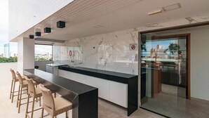 A modern kitchen with a marble backsplash, a black countertop, and a glass door leading to a dining area. - GOLDFLAT Manaíra by Penareia.tur.br (João Pessoa)