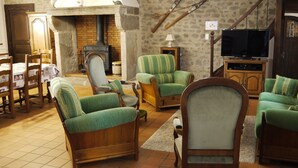 A cozy living room with a fireplace, green upholstered chairs, a wooden cabinet, and a television. - Gîtes au Château de Vernières (Talizat)