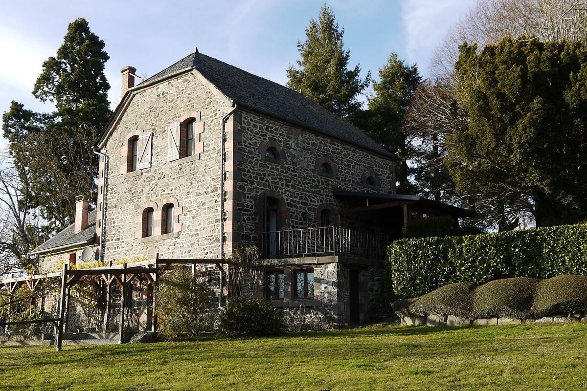 A stone building with a balcony, surrounded by trees and a well-maintained lawn.