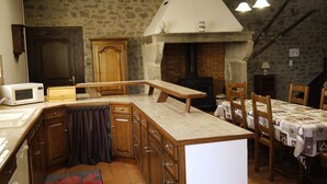 A kitchen with wooden cabinets, a microwave, a brick fireplace, and a dining table with chairs. - Gîtes au Château de Vernières (Talizat)