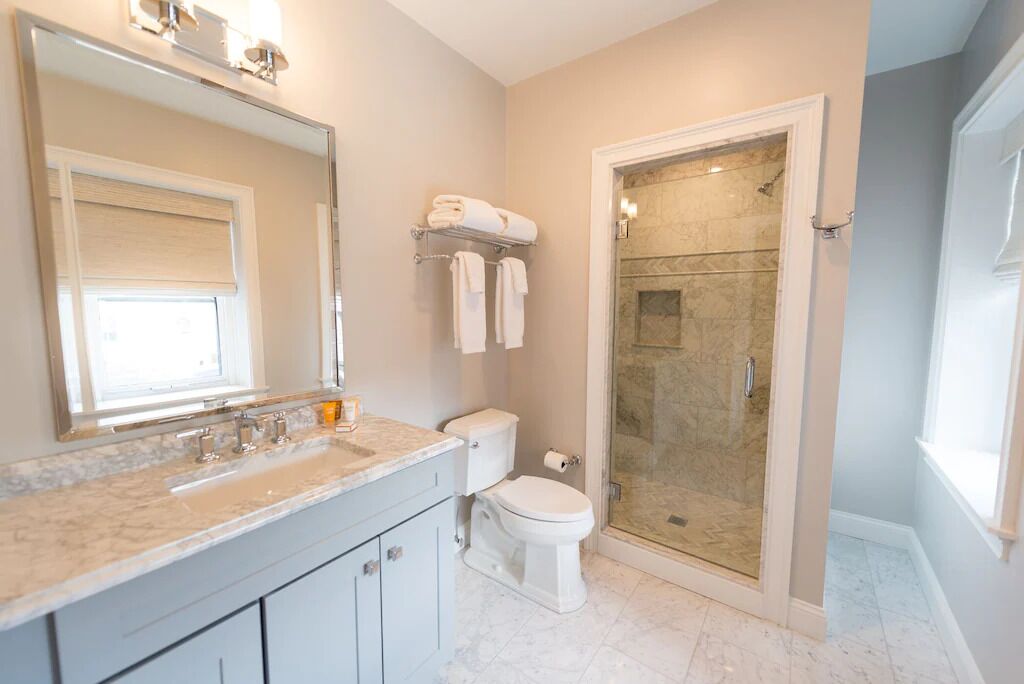 Un baño moderno con un espejo grande, un lavabo de mármol, inodoro y ducha con mampara de vidrio.
