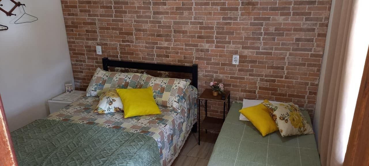 Une pièce avec un mur en briques, un lit avec une couette et des oreillers, une table de chevet et une petite table sur laquelle est posé un vase.