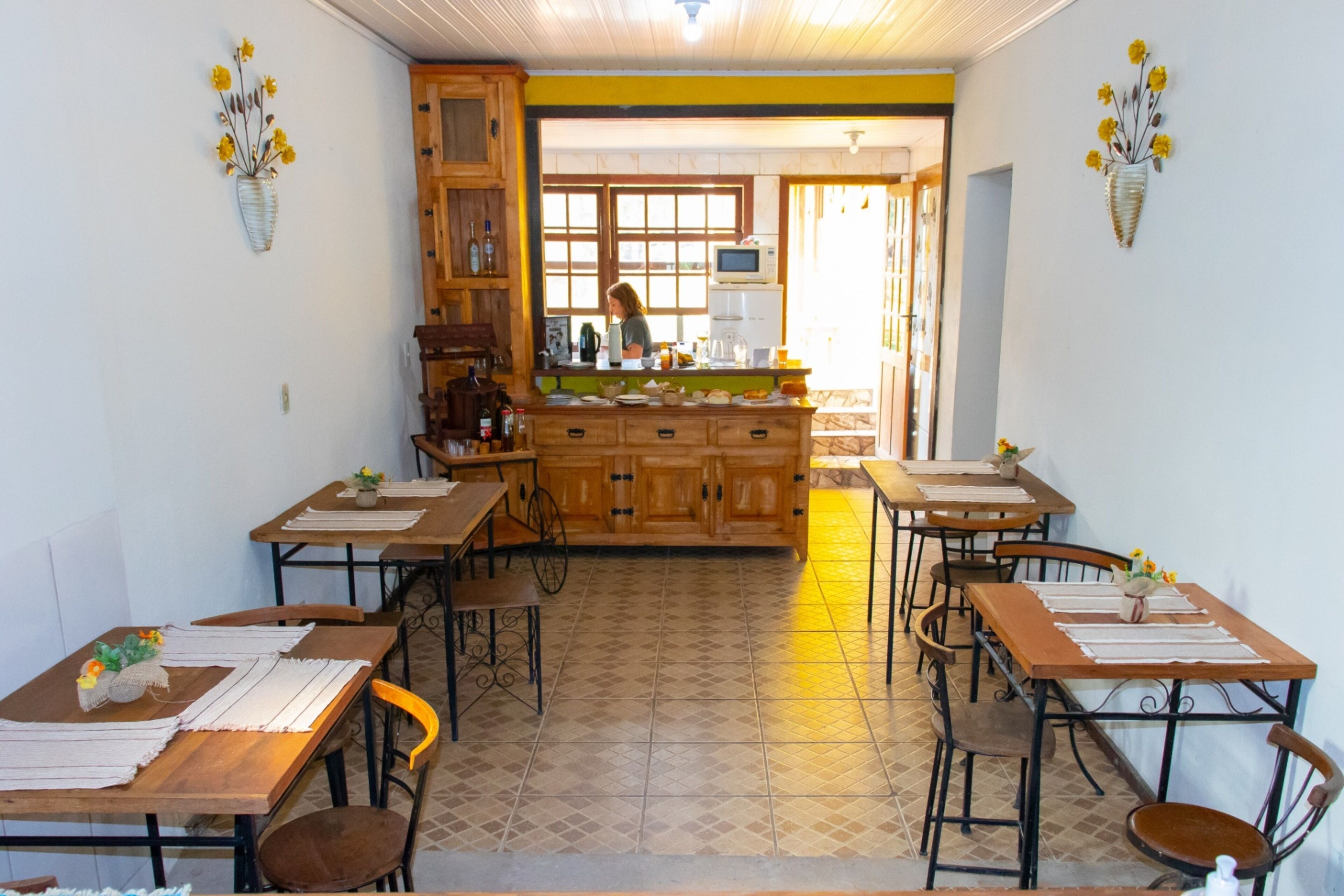 Un comedor con mesas y sillas de madera, una encimera de cocina central y jarrones decorativos en la pared.
