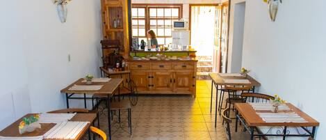 Un comedor con mesas y sillas de madera, una encimera de cocina central y jarrones decorativos en la pared.