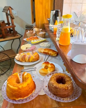 Et morgenbord med forskellige kager, en kaffemaskine og et kande appelsinjuice.