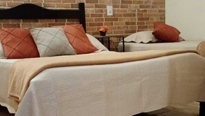 Een bed met een witte spreidek en een houten hoofdbord, met een bakstenen muur erachter.