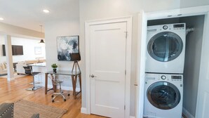 Un apartamento moderno con lavadora y secadora de dos fuegos, una mesa de vidrio con una silla y un cuadro en la pared.