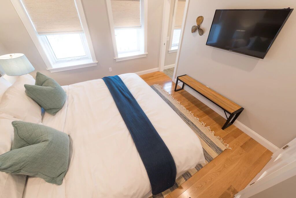 Une chambre à coucher avec un lit, des oreillers, un banc, une télévision et une fenêtre.