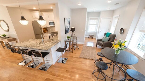 Una cocina moderna con una isla de mármol, un comedor con una mesa redonda y una sala de estar con sofá y mesa de centro.