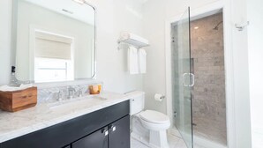Un baño moderno con cabina de ducha de vidrio, inodoro blanco y encimera de mármol.