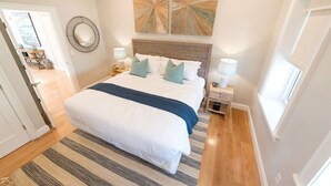 Un dormitorio con una cama grande, dos mesitas de noche con lámparas, un espejo redondo y arte abstracto en la pared.