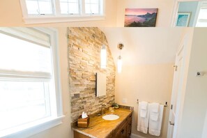 A bathroom with a stone wall, a wooden vanity, a sink, a mirror, and a window. - Dog Friendly Cottages w/ easy access to Newport, beaches, trails  and  vineyards (Middletown)