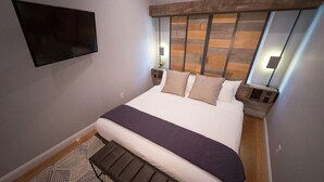 Una habitación de hotel moderna con una cama grande, un televisor montado y un cabecero de madera original.