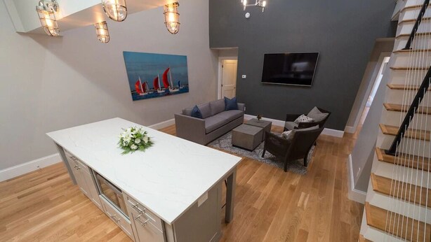 Un interior moderno con isla de cocina, sofá gris y suelo de madera.