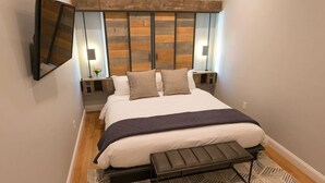 Un dormitorio moderno con una cama grande, cabecera de madera, lámparas de noche y un banco al pie de la cama.