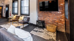 Ein modernes Wohnzimmer mit Backsteinwand, Flachbildfernseher, Sofa, Sessel und Kamin.