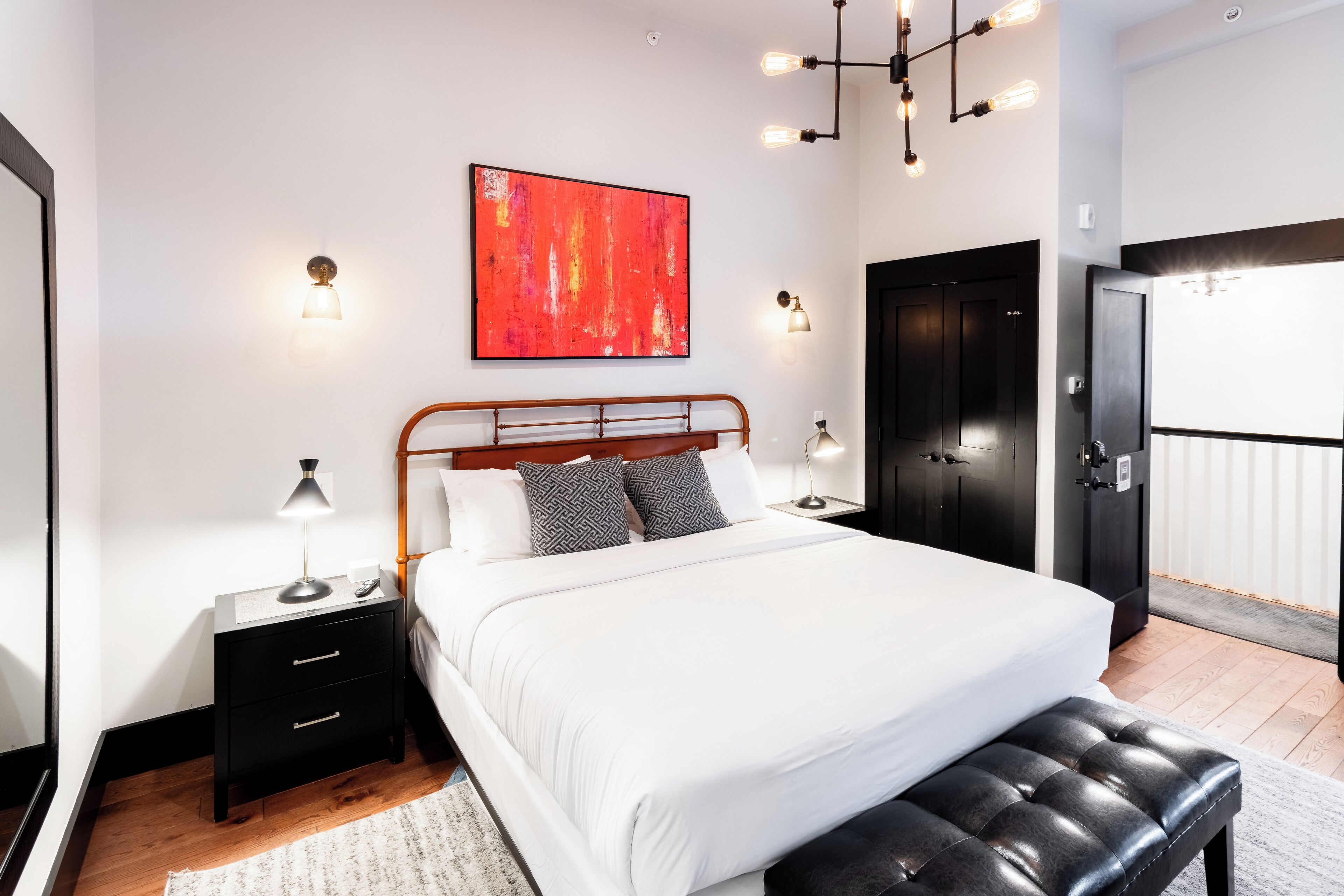 A modern bedroom with a large bed, a nightstand, a bench, and a wardrobe.