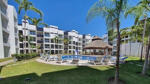 Ein modernes Gebäude mit Swimmingpool, Liegestühlen und Palmen.