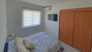 Ein Schlafzimmer mit einem Bett, einem Fenster mit Jalousien, einer Klimaanlage und einem Holzschrank.